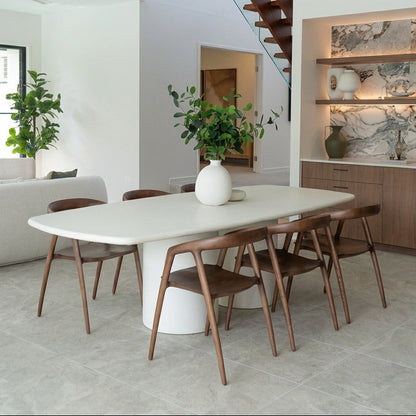 Modern dining area with a white table and wooden chairs in a bright room.