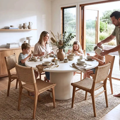 Family of four sitting around a white dining table in a bright room with large windows.