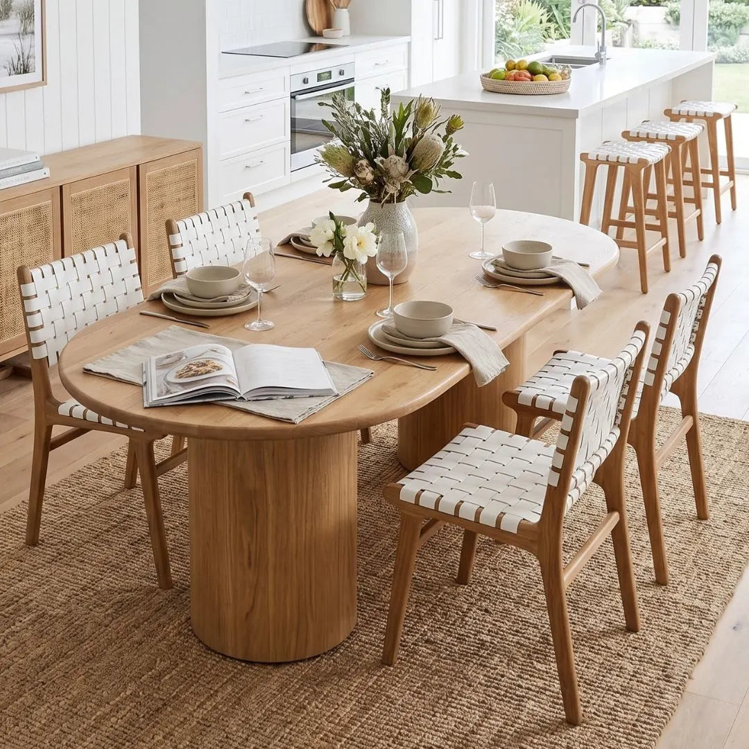 Dining room with wooden table and chairs, books, and flowers.
