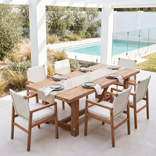 A 7-piece outdoor dining set featuring a rectangular wooden table and six matching armchairs with white woven rope seats, set on a patio next to a swimming pool.