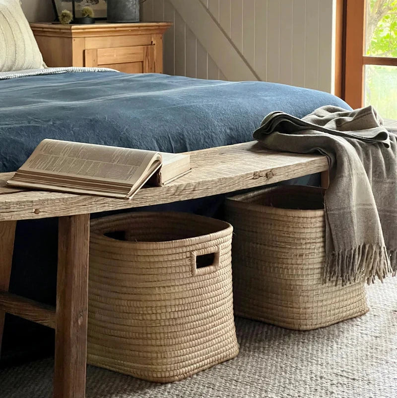 Cozy bedroom with wooden bench, blue bedding, and woven baskets.
