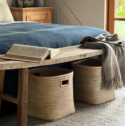 Cozy bedroom with wooden bench, blue bedding, and woven baskets.