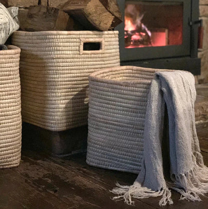 Woven baskets with a blanket in front of a stone fireplace.