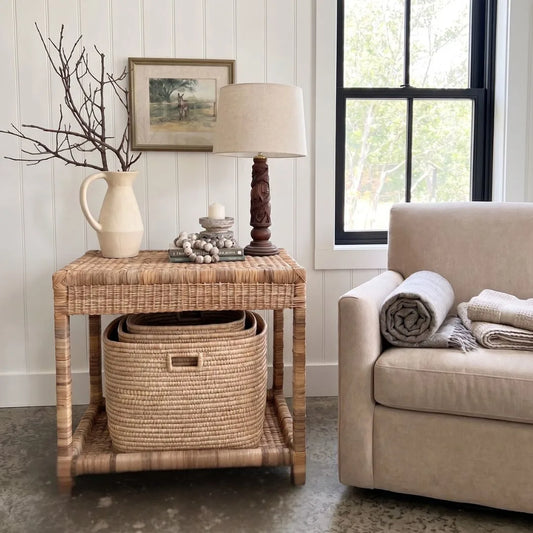 Wicker side table with lamp, basket, and decorative items next to a beige sofa.