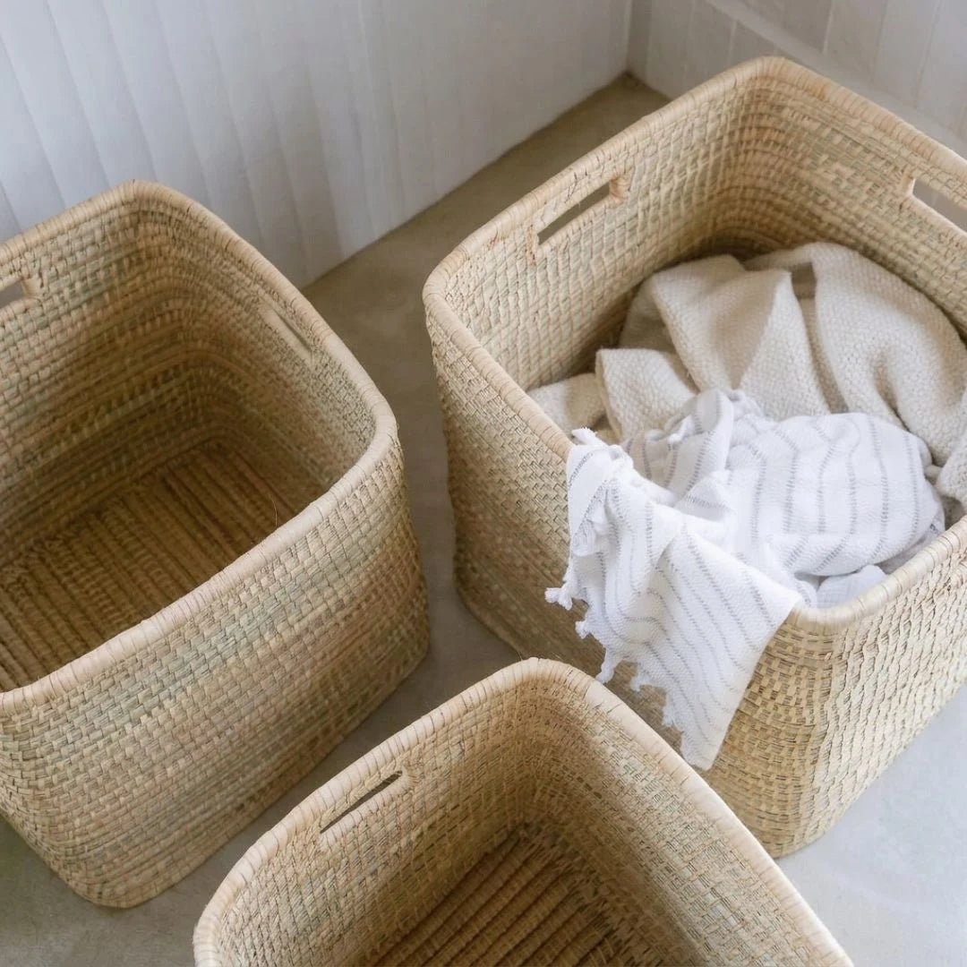 Three woven baskets on a light-colored floor with one containing white towels.
