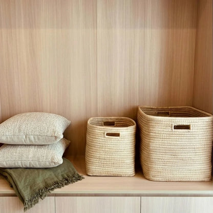 Woven baskets and pillows on a wooden shelf against a striped wall.