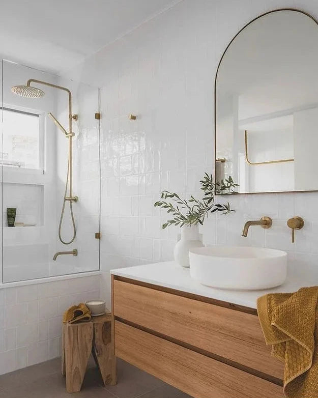 Modern bathroom with teak peg stool, wooden vanity, white sink, and gold fixtures.