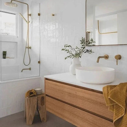 Modern bathroom with teak peg stool, wooden vanity, white sink, and gold fixtures.