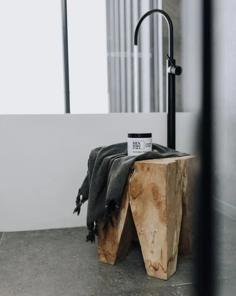Square teak peg stool with a towel and a jar on it in a bathroom setting.