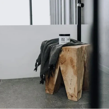 Square teak peg stool with a towel and a jar on it in a bathroom setting.