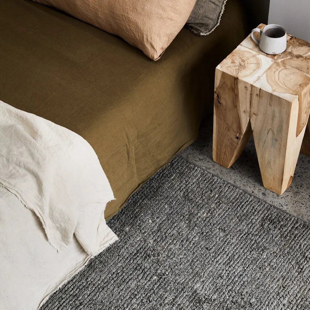 Square teak side table next to a bed 