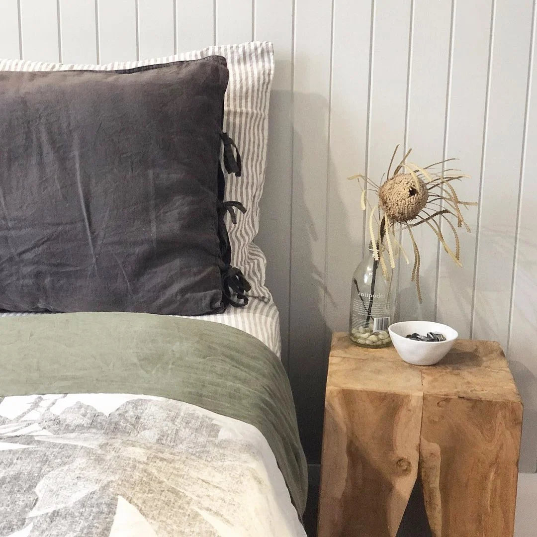 Square teak side table next to a bed 