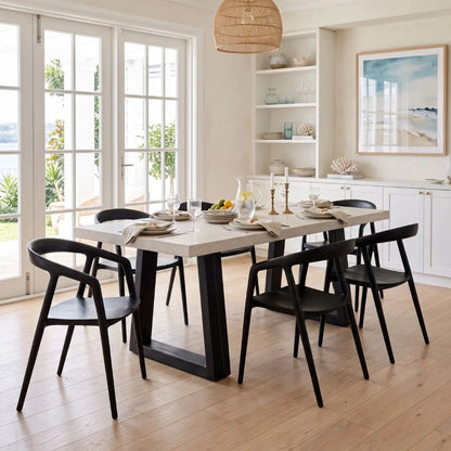 Modern dining room with a long wooden table and black chairs, large windows, and a beach-themed painting.
