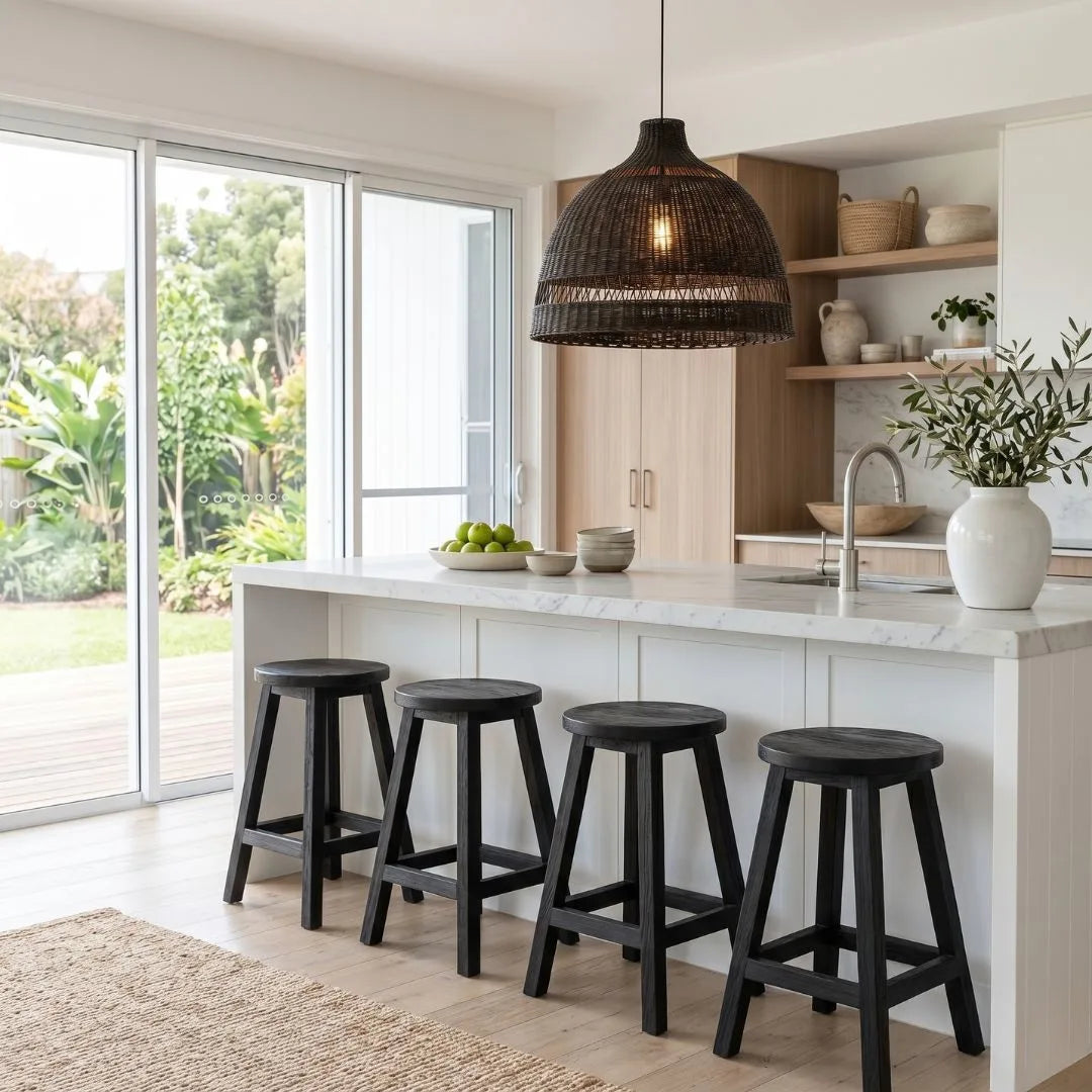 Round black teak stools at a kitchen island bench with a black woven cane pendant in a modern kitchen