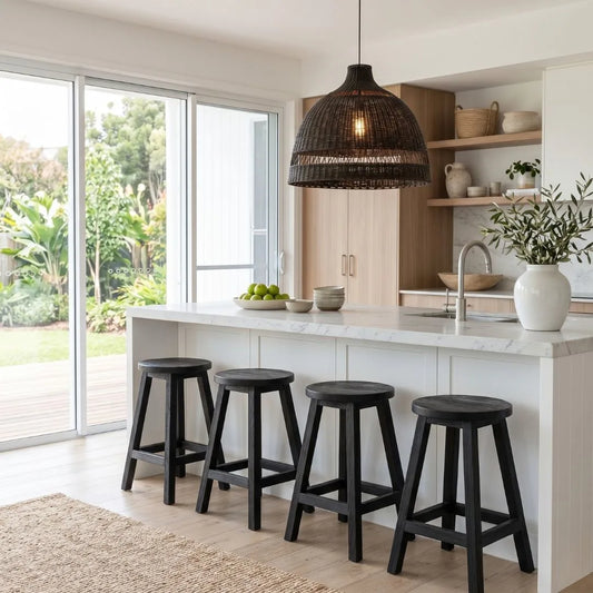 Round black teak stools at a kitchen island bench with a black woven cane pendant in a modern kitchen