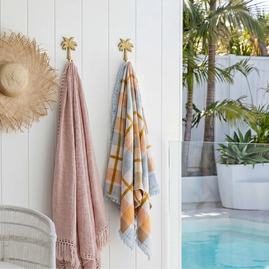 Towels hanging on a wall next to a pool with palm trees and plants.