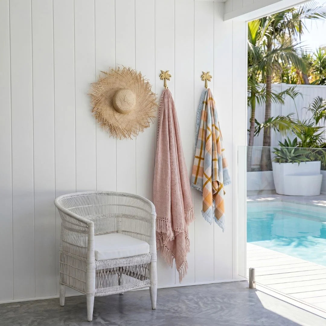Wicker chair with a straw hat and beach towels by a poolside.