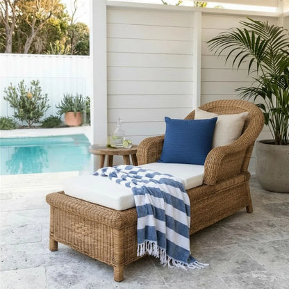 Wicker chair with cushions and a blue and white striped blanket by a poolside.
