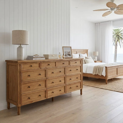 Wooden dresser in a bedroom with a bed and lamp in the background