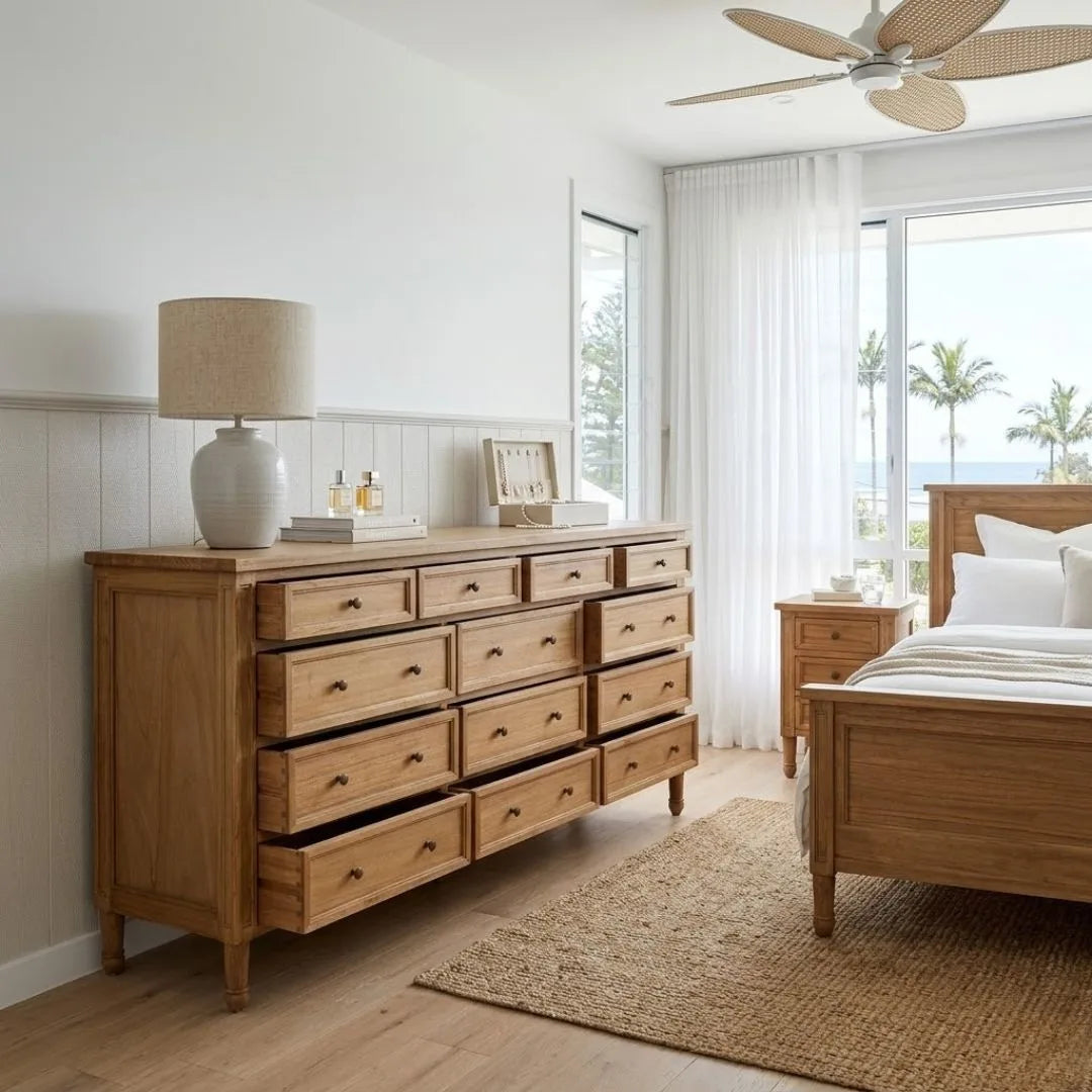 Wooden dresser in a bedroom with a bed and lamp in the background