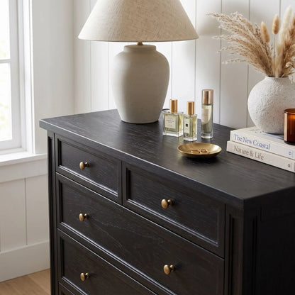 Dark wooden dresser with decorative items including a lamp, books, and bottles on a light wood floor.