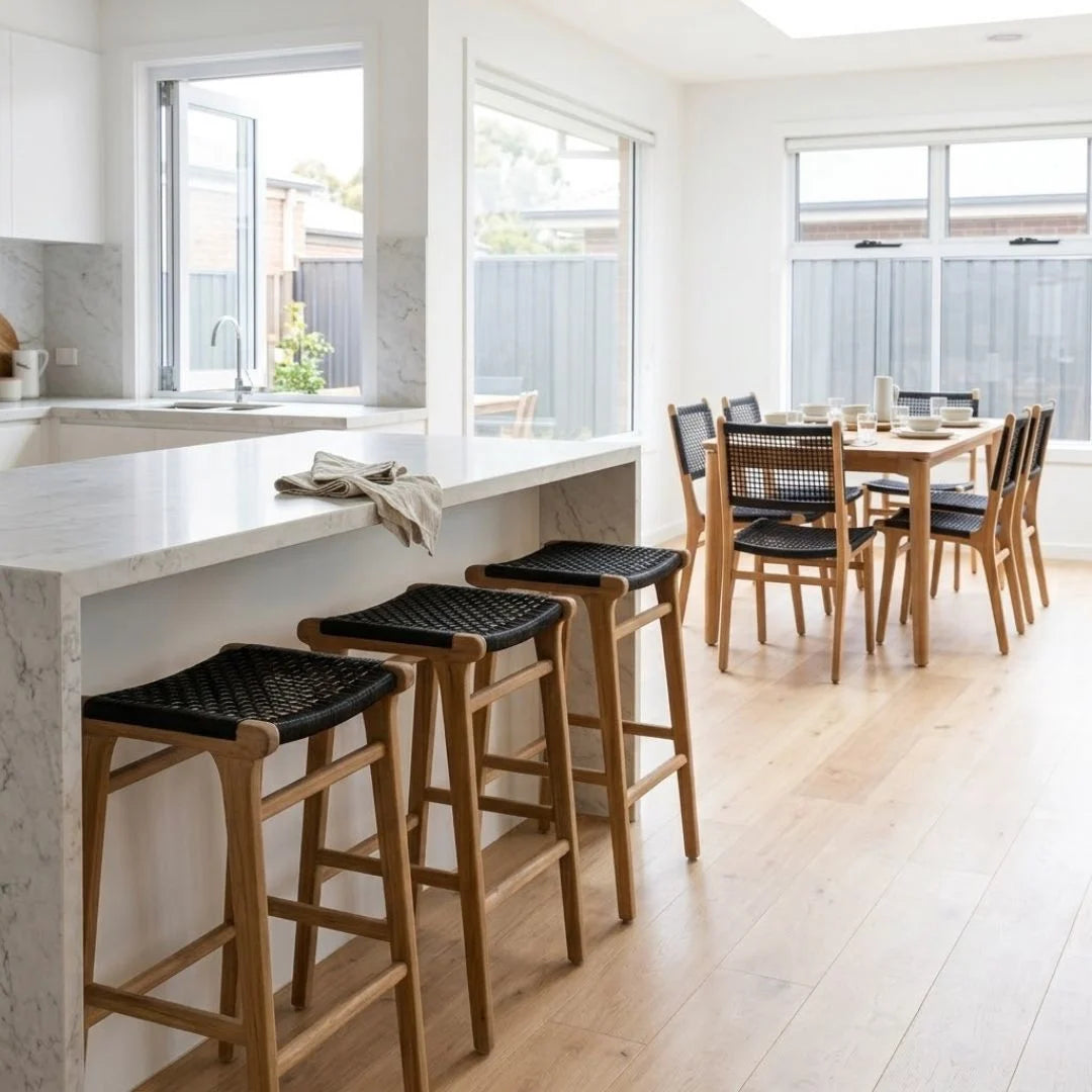 A set of four wooden bar stools with black woven seats, shown in a bright, modern kitchen and dining area.