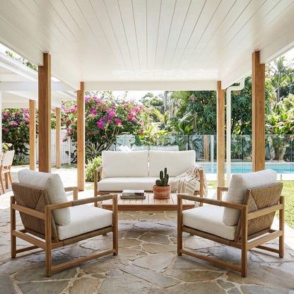 Outdoor patio set with wooden chairs and table on a stone patio, surrounded by greenery.