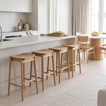 Wooden bar stools in a modern kitchen setting with white countertops and neutral decor.