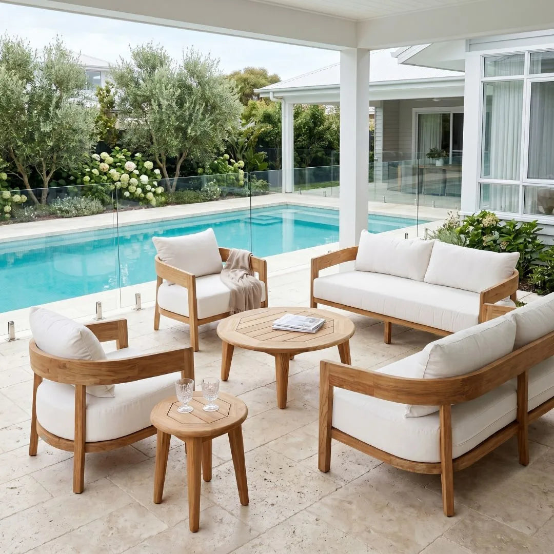 Outdoor patio furniture set with wooden frames and white cushions by a pool.