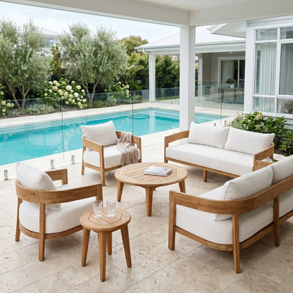 Outdoor patio furniture set with wooden frames and white cushions by a pool.