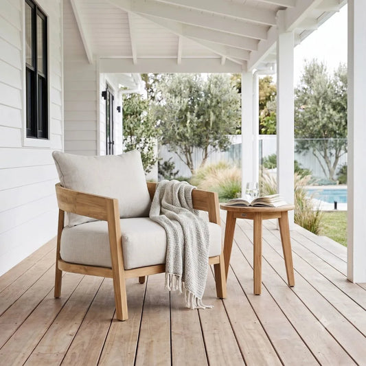 Wooden chair with white cushion and blanket on a wooden deck with a view of trees and pool.