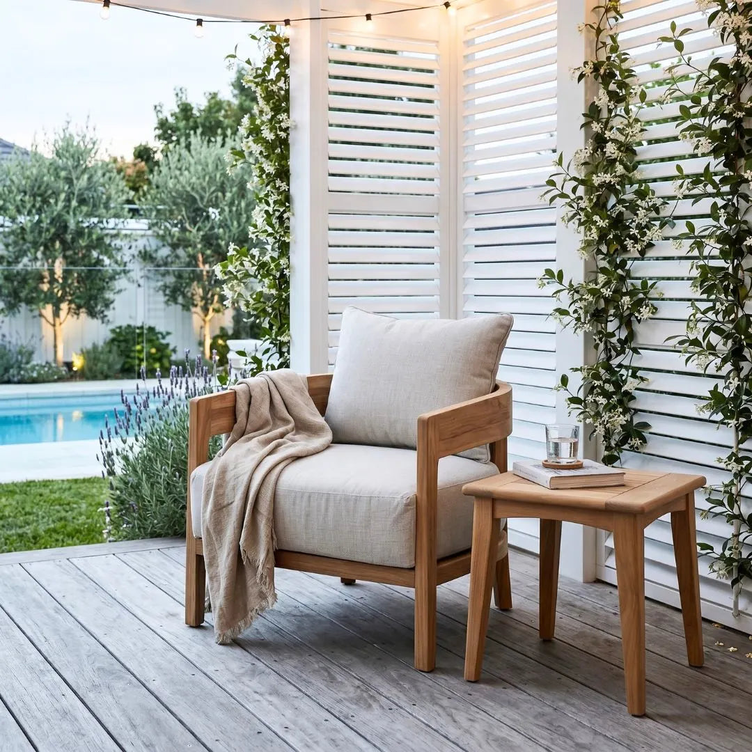 Wooden chair with beige cushions and a blanket on a wooden deck by a poolside.