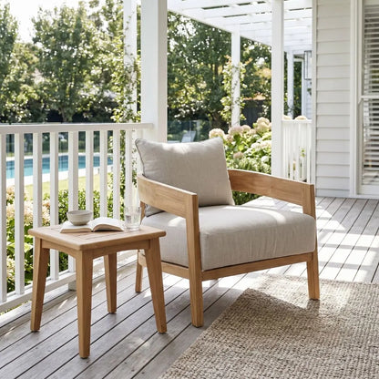 Wooden armchair with beige cushion on a porch with a small table and book.