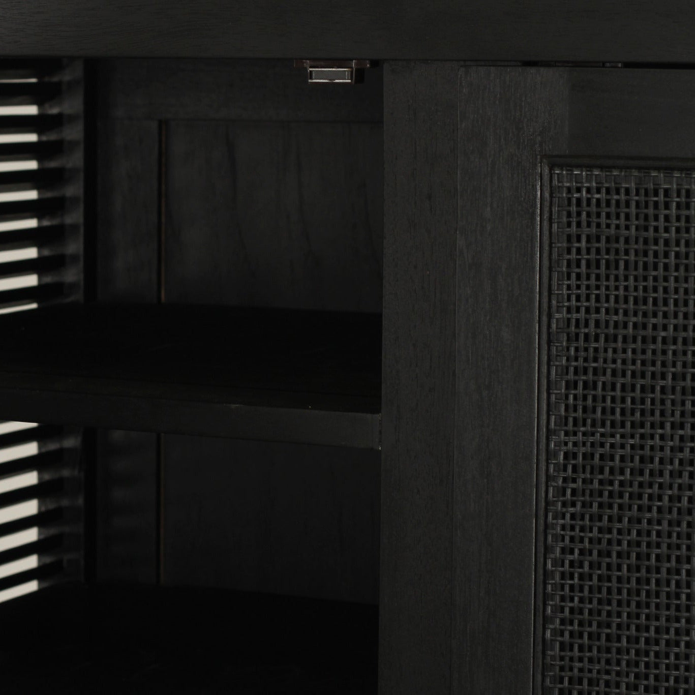 Close-up of the interior of a black storage cabinet, showing a slotted shelf, mesh panel on the right side.