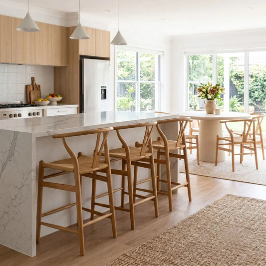 Modern kitchen with marble island, wooden bar stools, and large windows.