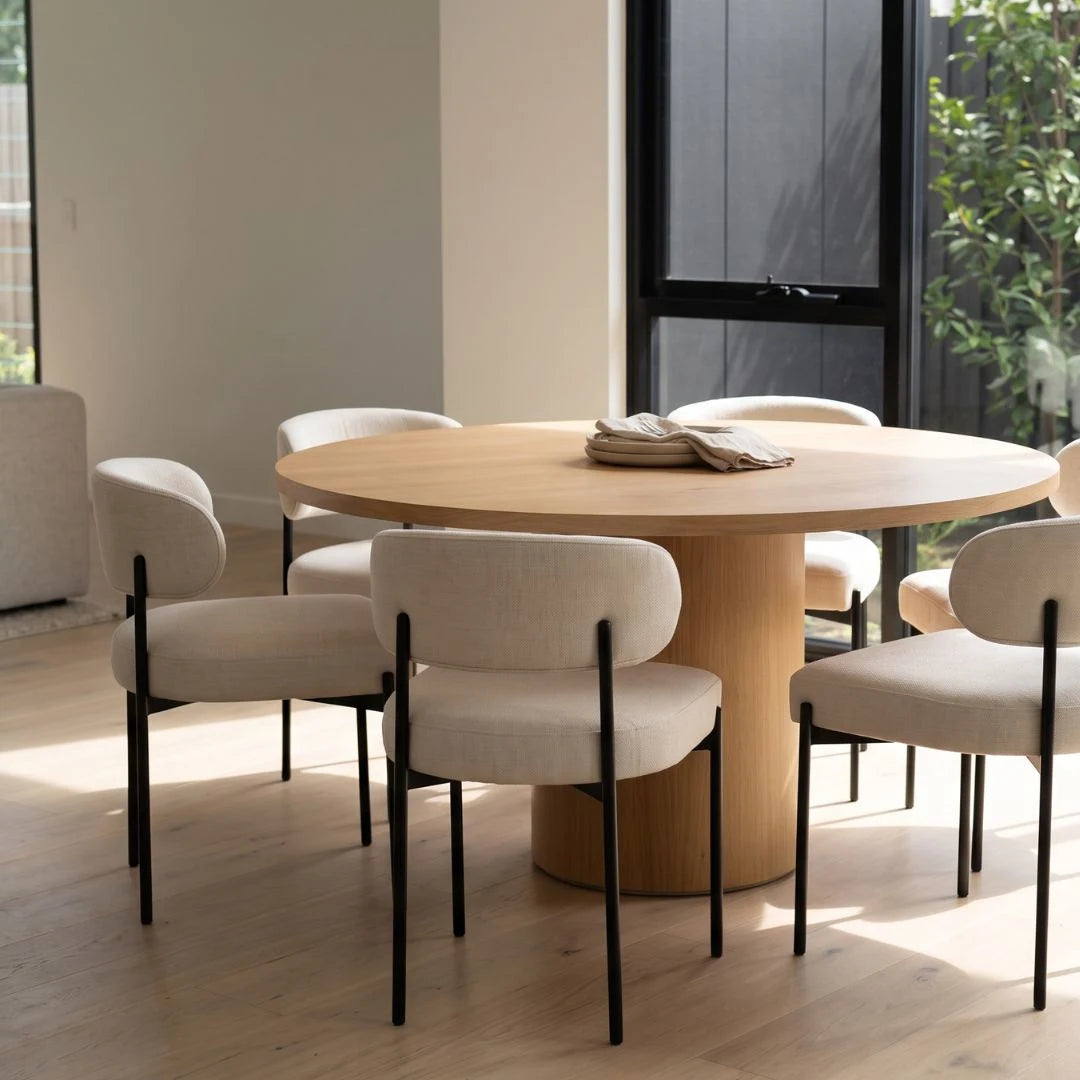Round wooden dining table with white chairs in a modern room.