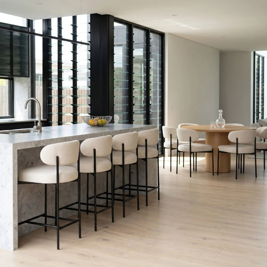 Modern kitchen with island and stools, large windows, and dining area.