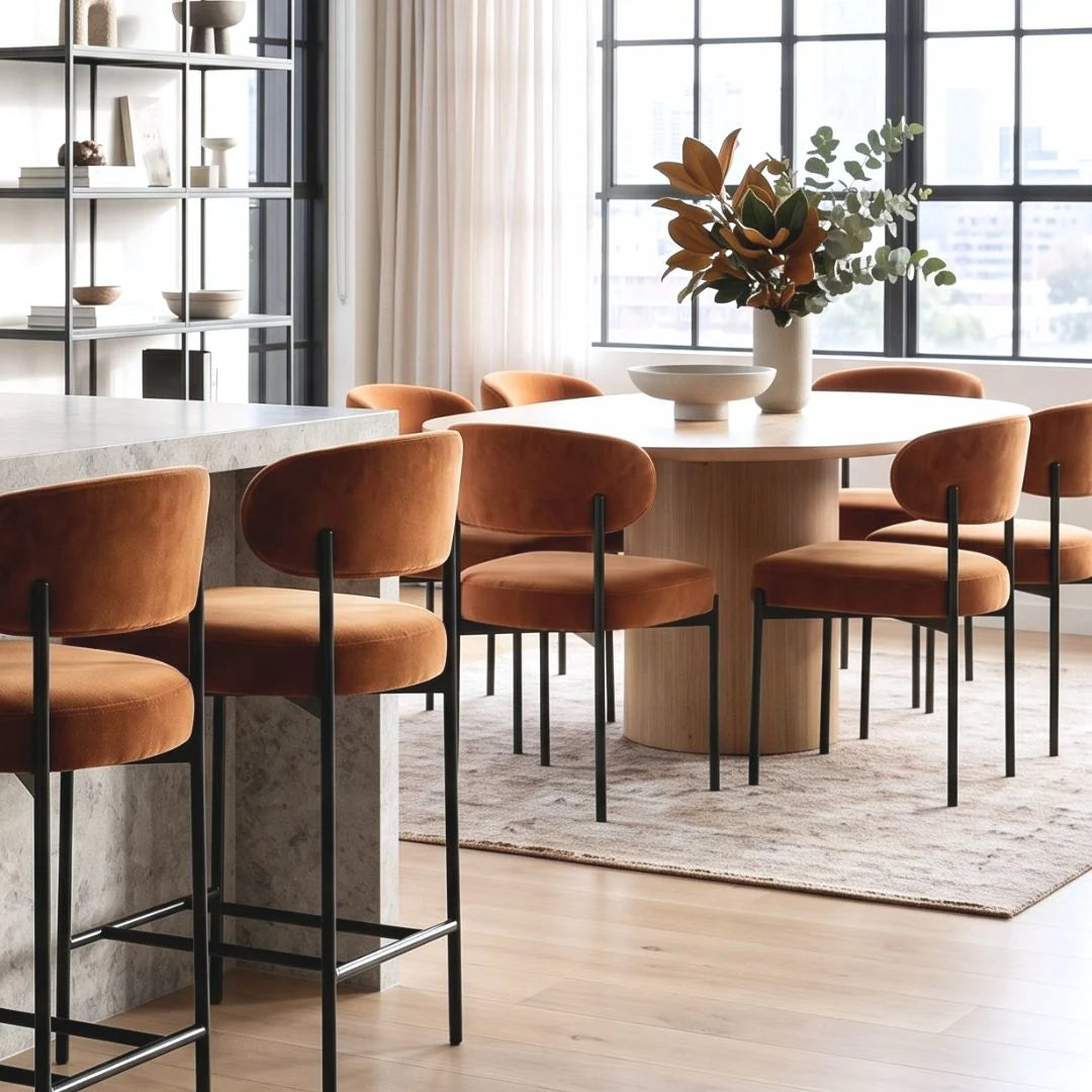 Dining room with round table and orange chairs near a large window.