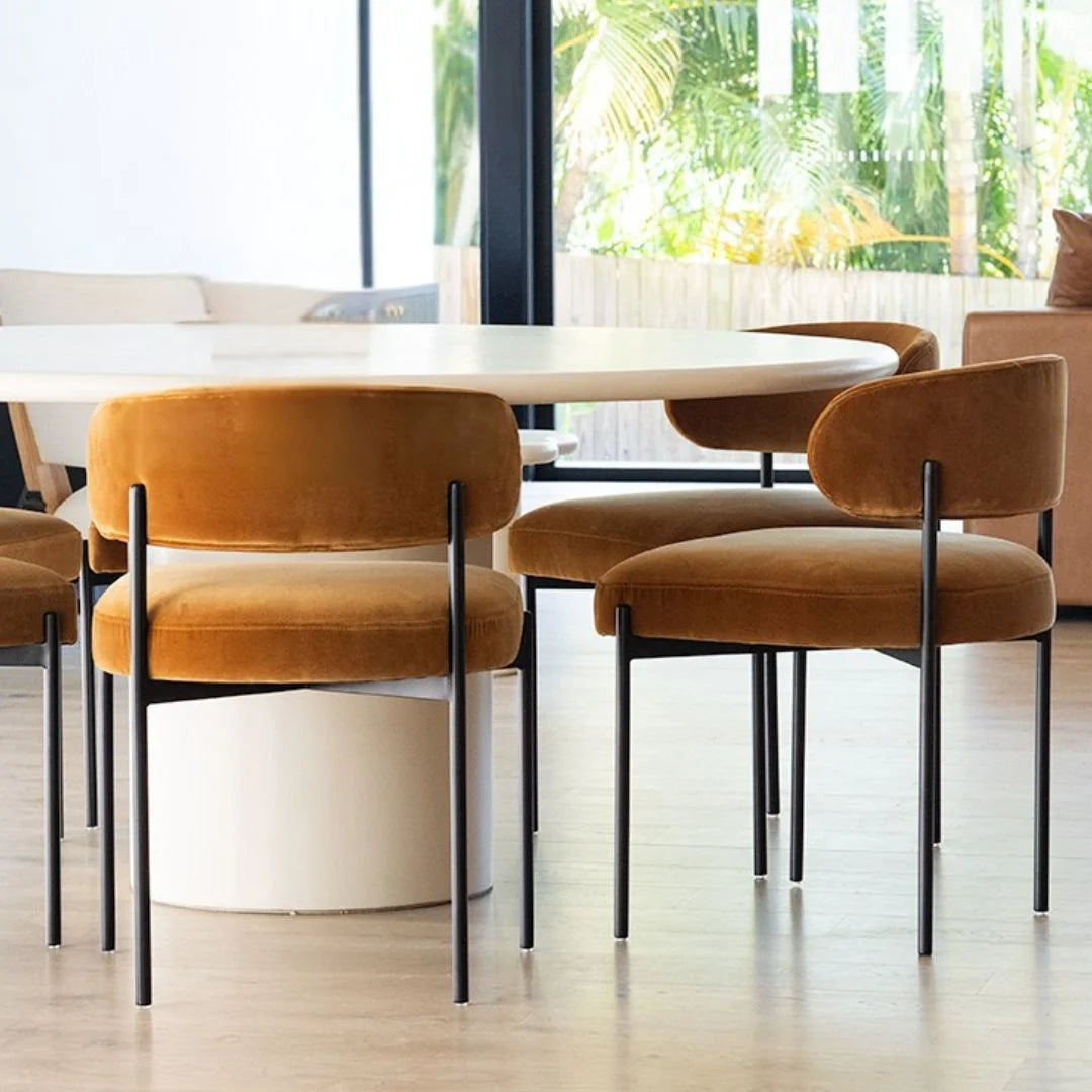 Dining table with brown chairs in a bright room with large windows.