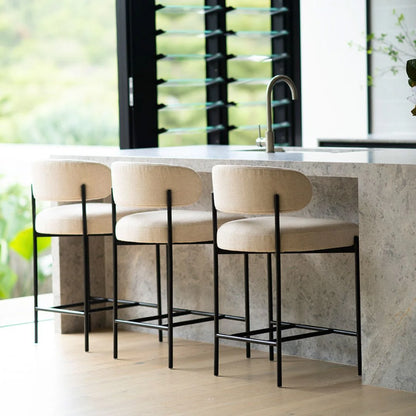 Three beige cushioned bar stools with black metal legs in a modern kitchen setting.