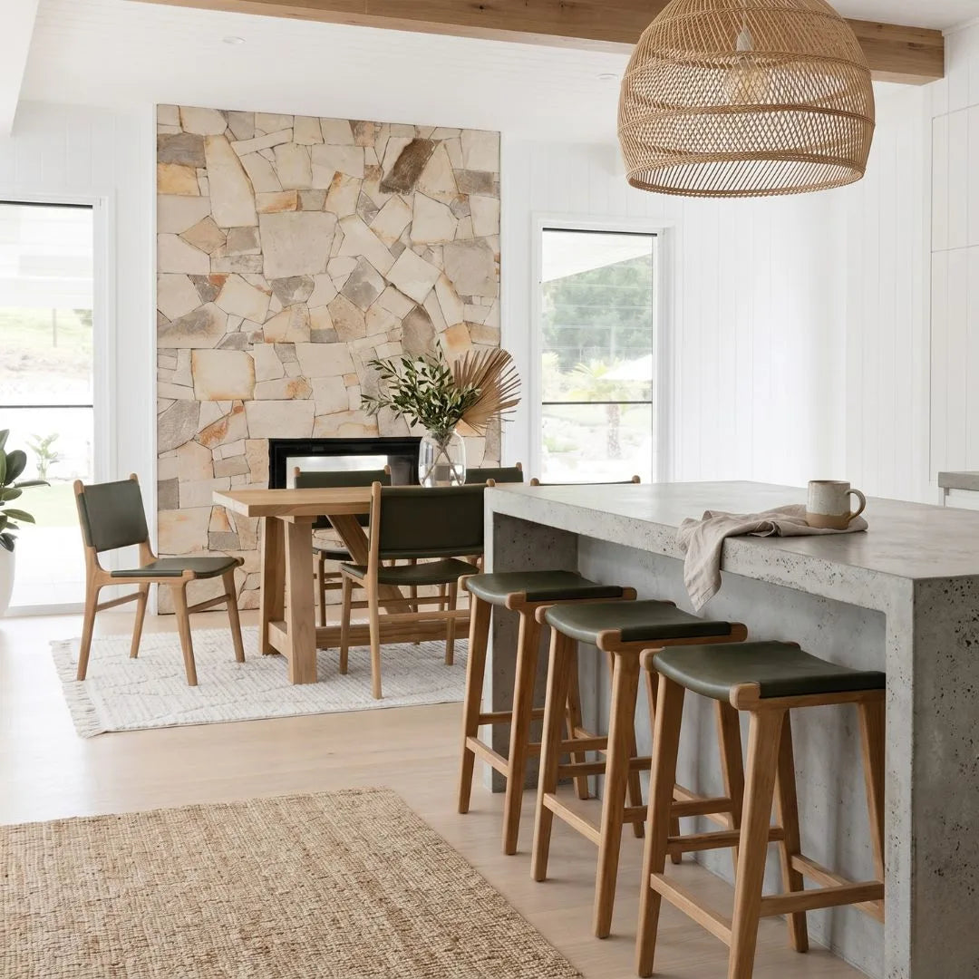 Modern kitchen with concrete island, bar stools, and a stone wall.