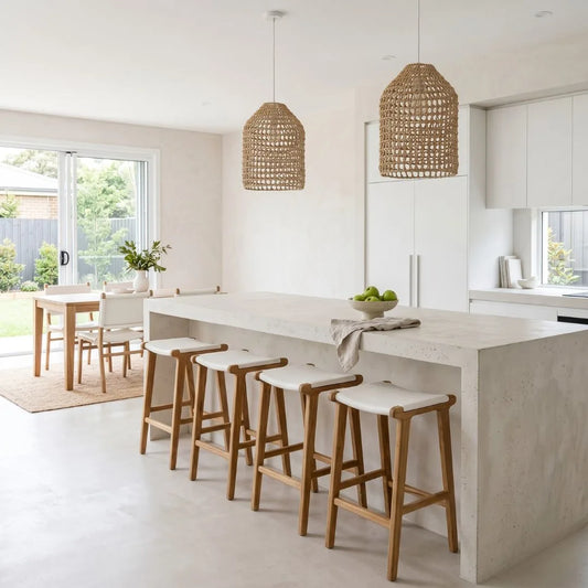 Modern kitchen with white island bench with white leather and teak counter stools and rattan pendants