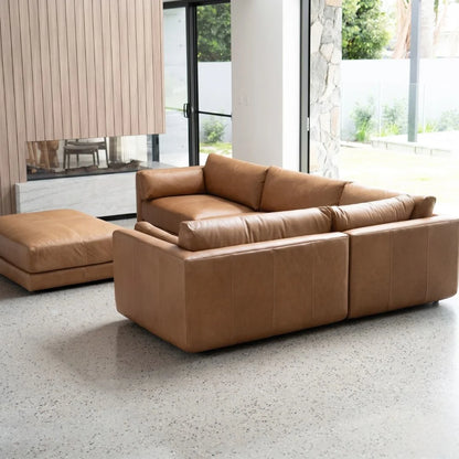 Brown leather sectional sofa in a modern living room with large windows.