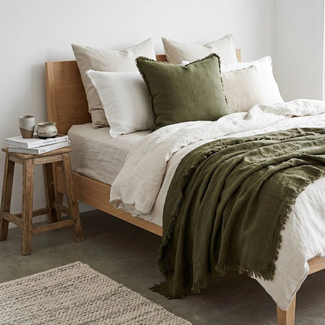 Bedroom with wooden bed, green and white bedding, and a wooden stool with books.
