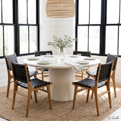 Dining room with a round white table and black chairs with wooden frames.