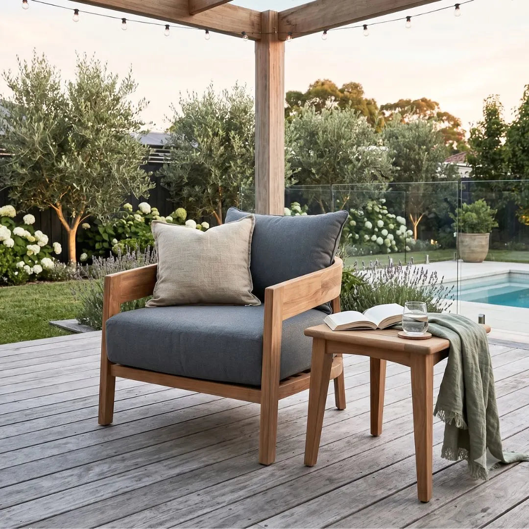 Outdoor seating area with a wooden chair and table on a deck, featuring a pool and garden in the background.