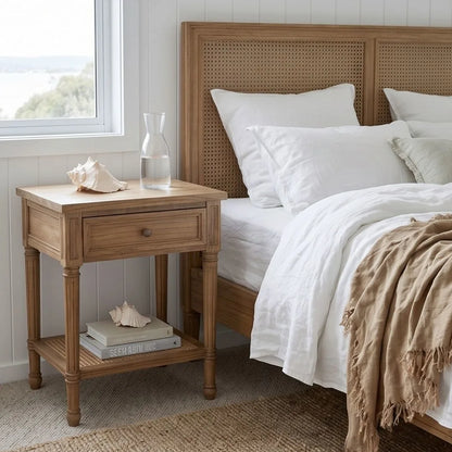 Wooden nightstand next to a bed with white bedding and a woven headboard.