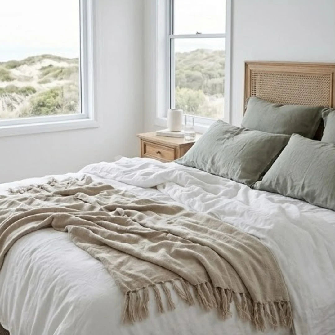 Neatly made bed with beige blanket and green pillows in a room with large windows showing a scenic view.