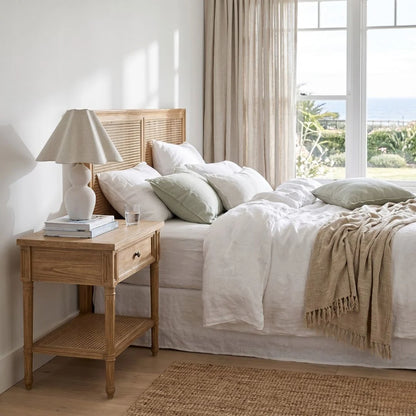 Bedroom with wooden bedside table, lamp, and bed with white linens and green pillows.