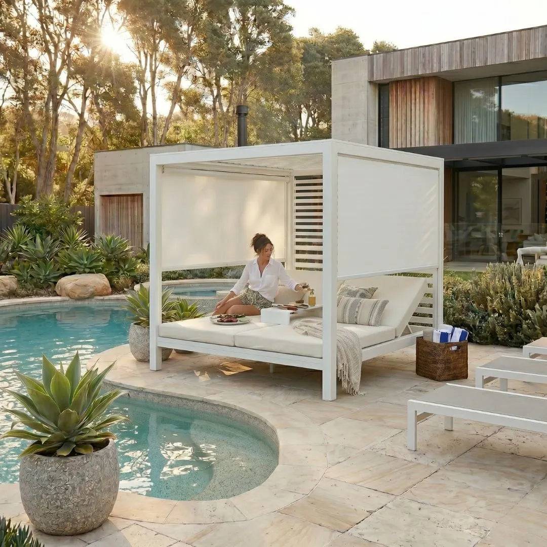 Person sitting on a daybed cabana under a white canopy by a poolside.